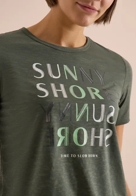 Frau trägt olivgrünes T-Shirt mit Aufdruck „SUNNY SHORE“ und gespiegeltem Schriftzug.